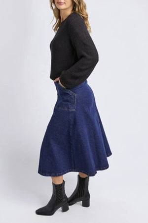 A person wears the Foxwood Blair Long Sleeve Knit in black, a blue flared 100% cotton denim midi skirt with side pockets, and black ankle boots, standing sideways against a plain light background.