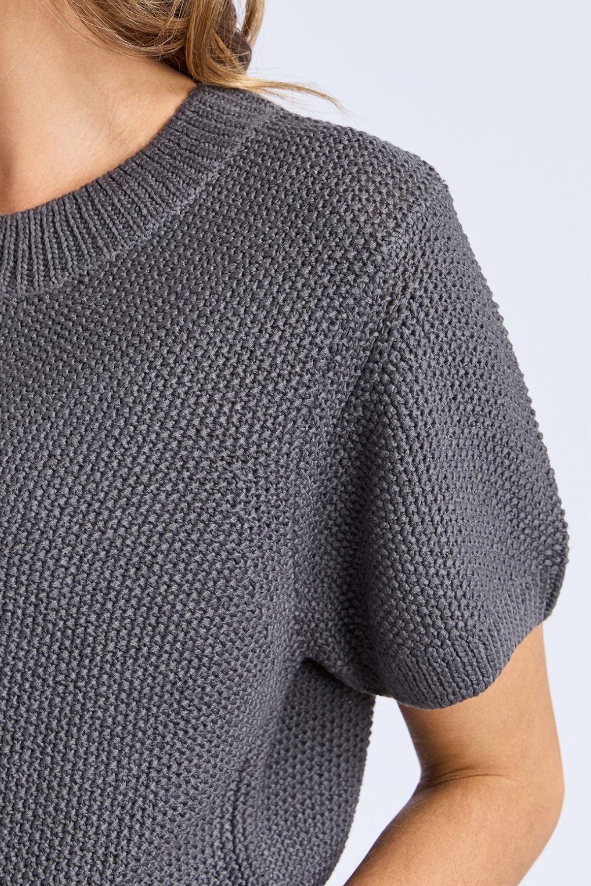 Close-up of a person wearing the Foxwood Blair Short Sleeve Knit, showing its detailed knit pattern and relaxed fit on the upper chest and arm, with light brown hair visible at the top.