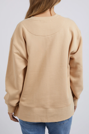 A person with light brown hair is standing with their back to the camera, wearing a Foxwood Carnation Crew jumper in a relaxed fit made of 100% cotton, paired with blue jeans. The background is plain and light gray.
