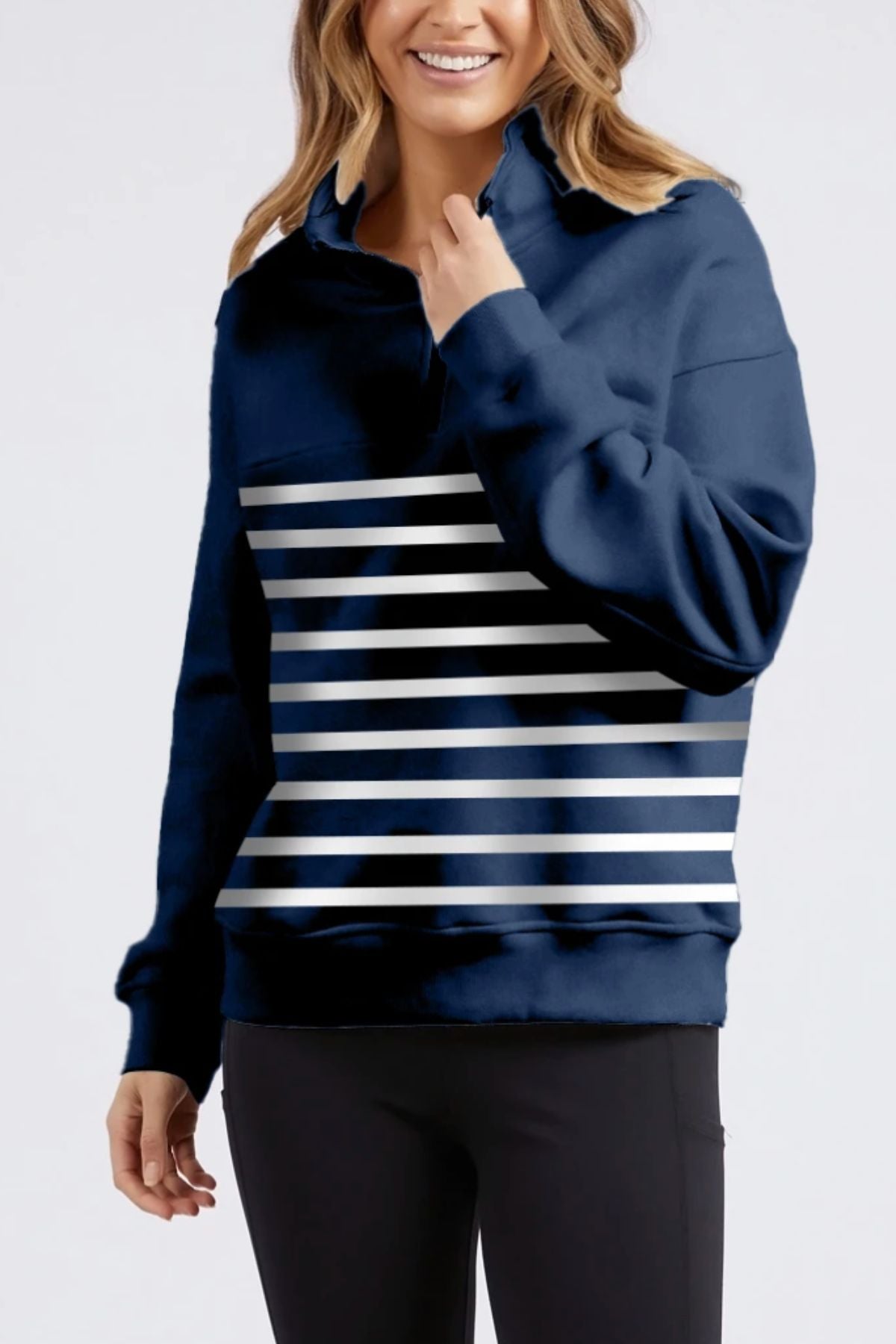 A woman is smiling and holding the collar of a navy blue Foxwood College Zip Crew with horizontal white chest stripes and black pants, highlighting the crewβs relaxed fit.