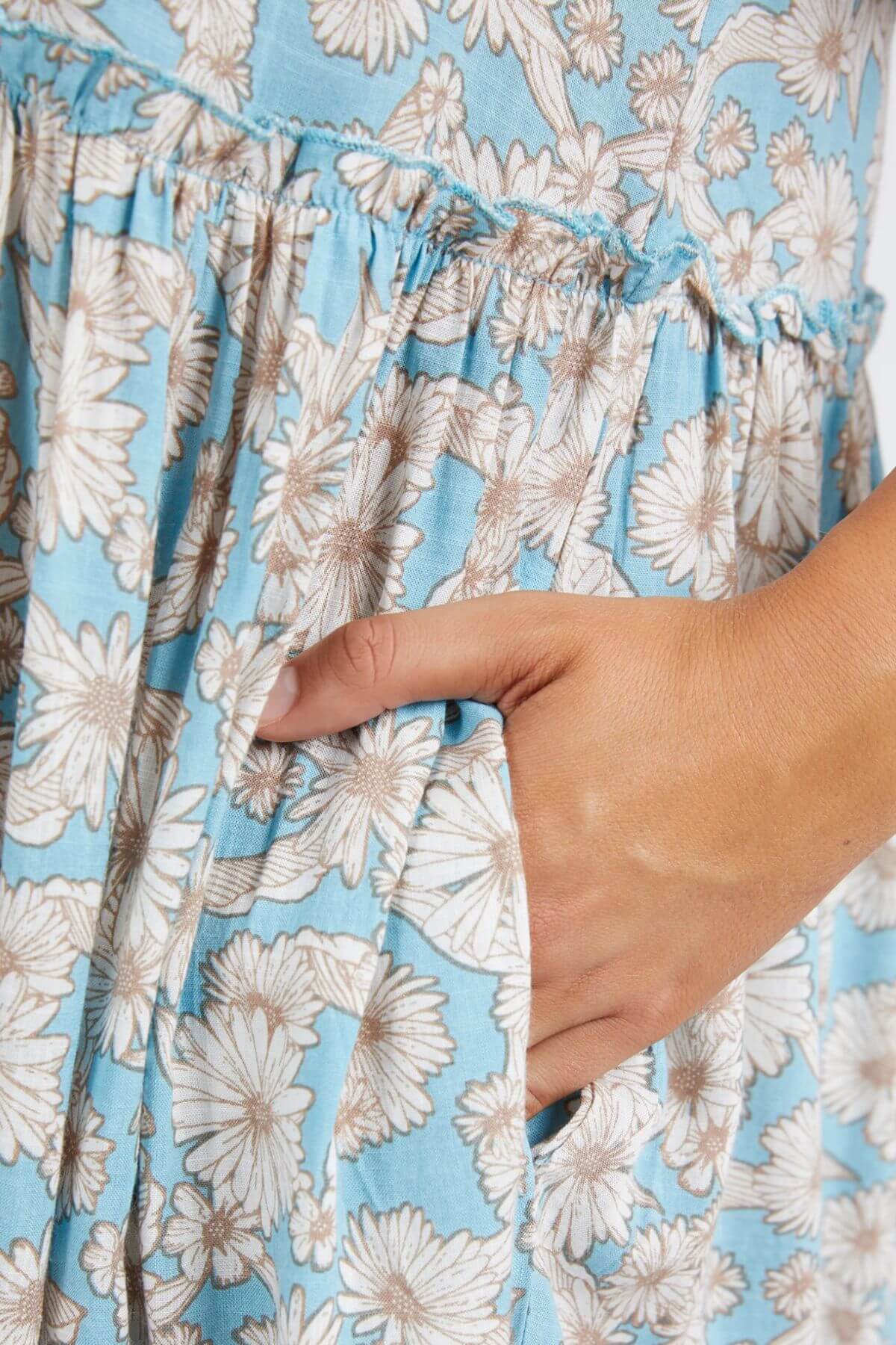 Close-up of a hand in the pocket of a Foxwood Daisy Dress, showcasing its gathered waist, soft light viscose fabric, white daisy pattern, and elegantly flowing tiered skirt.