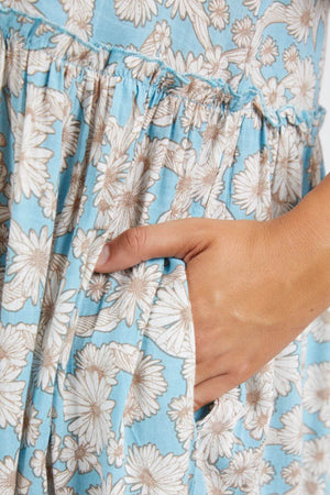 Close-up of a hand in the pocket of a Foxwood Daisy Dress, showcasing its gathered waist, soft light viscose fabric, white daisy pattern, and elegantly flowing tiered skirt.