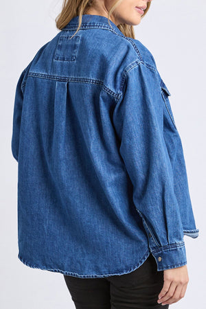 A person is shown from the back wearing a relaxed fit Foxwood Daisy Overshirt styled as an oversized blue denim jacket with black pants, featuring visible seams and buttoned cuffs, their head turned slightly to the side.