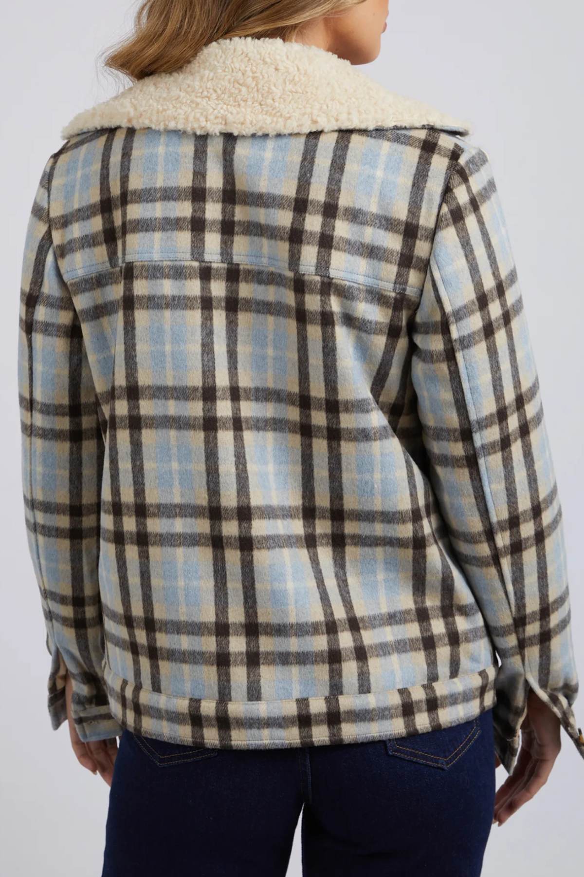 A person seen from the back wears the Foxwood Demi Check Jacket in blue, beige, and brown checks with a cream sherpa lining, paired with dark blue jeans.