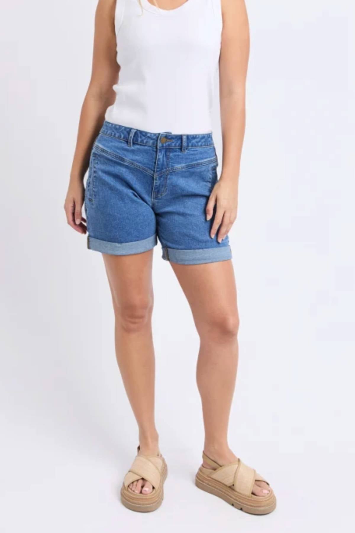 A woman wearing a sleeveless white top, Foxwood Devi Short, and beige platform sandals stands against a plain light background, arms relaxed by her sides. Her head is not visible in the image.