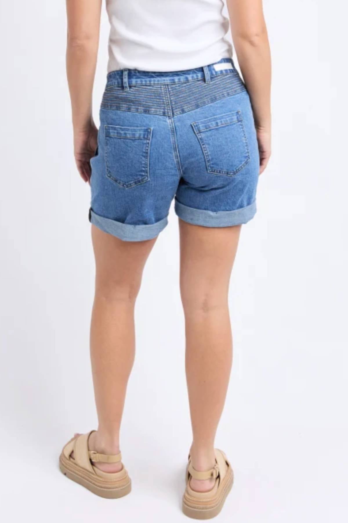 A person stands with their back to the camera, wearing a white top, Foxwood Devi Short in rolled-up blue denim, and beige platform sandals against a plain white background.