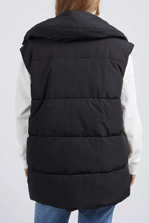 A person, facing away, wears the Foxwood Essential Puffer Vest made of durable polyester with horizontal stitching and a wide collar over a white long-sleeve shirt and blue jeans against a plain white background.