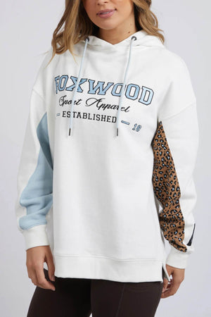 Wearing a relaxed fit, white Foxwood Established Hoody featuring "Sport Apparel" on the front and blue/leopard-print sleeve patches, a person with long wavy hair is paired with dark pants.