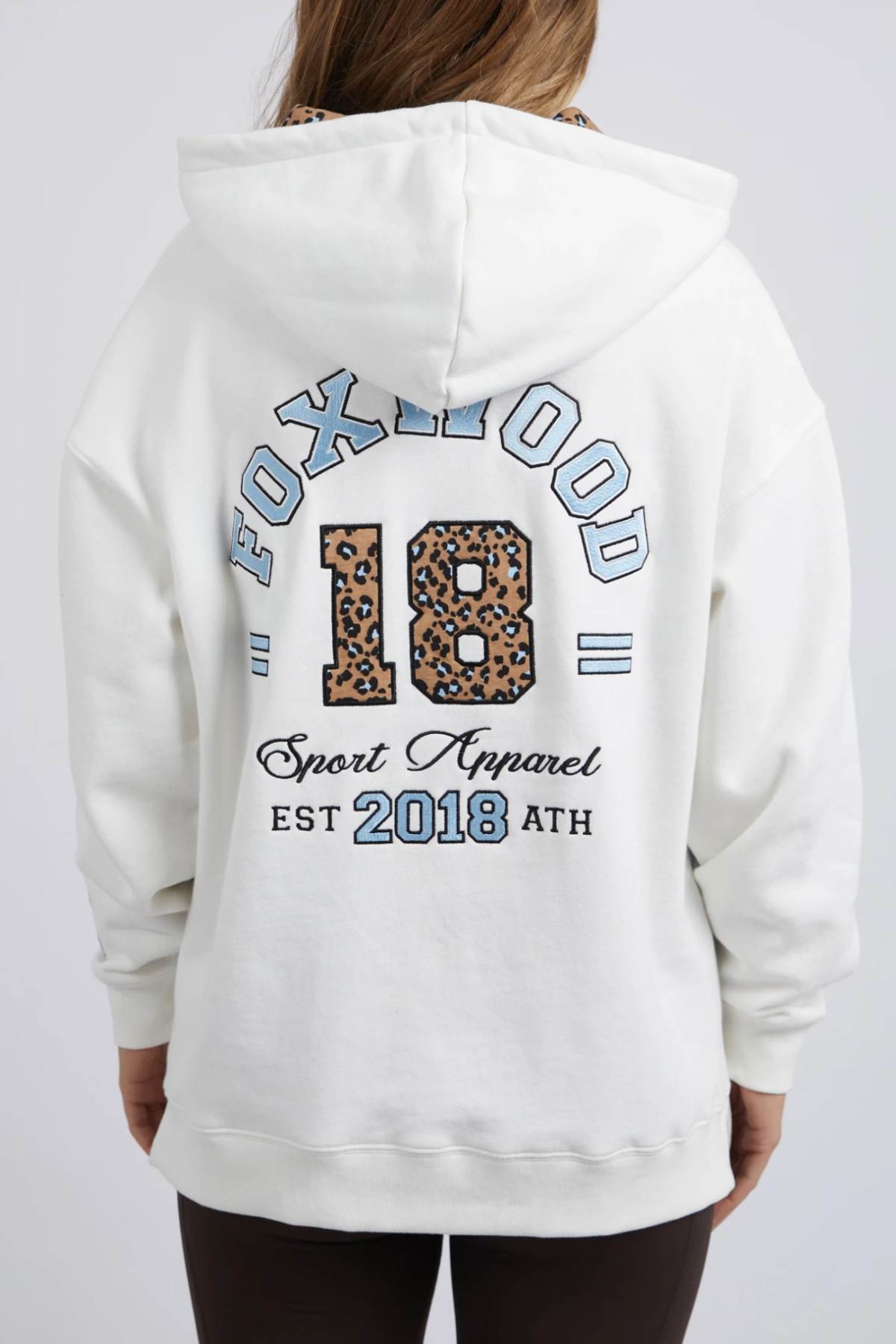The Foxwood Established Hoody is a relaxed fit, white hoodie featuring "FOXWOOD 18" in blue and leopard print across the back, "Sport Apparel EST 2018 ATH" below, chest embroidery, and long sleeves.