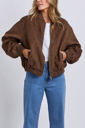 A woman stands with her hands in the pockets of a loose Foxwood Evie Suede Bomber over a white top and high-waisted blue jeans, posed against a plain light background.