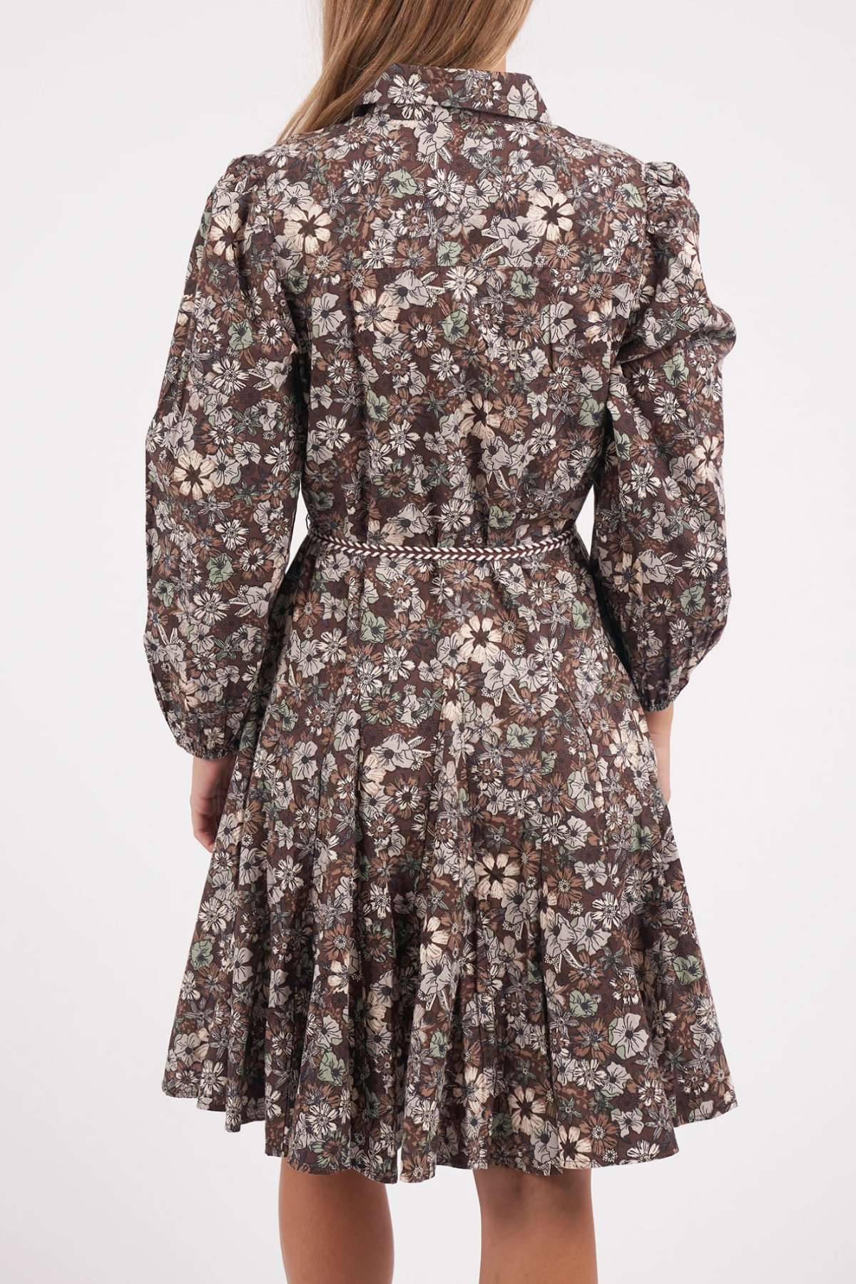 A woman with straight, light brown hair is seen from the back wearing a knee-length Foxwood Floral Meadow Dress featuring a brown floral print, long sleeves, a fitted drawstring waist, and a flared skirt.