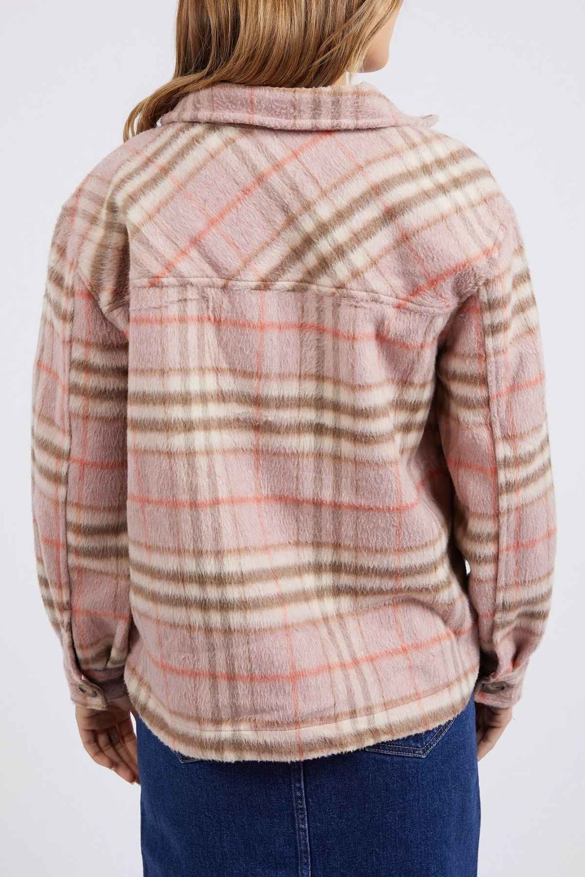 A person wearing a Foxwood Frankie Check Coat in pink, brown, and beige tones stands with their back to the camera. They are also sporting a dark blue denim skirt. The coat boasts a soft, textured appearance.
