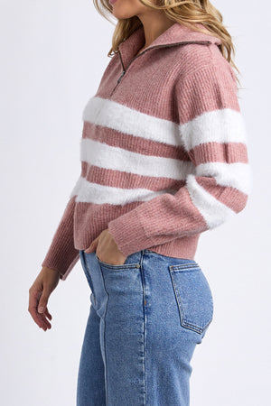 A woman wearing the Foxwood Gracie Zip Crew, a pink and white striped knit zip-neck sweater, with blue jeans stands with one hand in her pocket against a plain background.