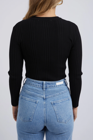 Seen from behind against a white background, a person wears the Foxwood Greta Long Sleeve in black, crafted from soft rib fabric for comfort and durability. Paired with high-waisted light blue jeans featuring two back pockets, the individual has long, light brown hair.