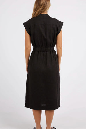 A woman with long hair is wearing a black, sleeveless Foxwood Harlow Midi Dress featuring a gathered waist. She stands with her back to the camera against a plain white background.