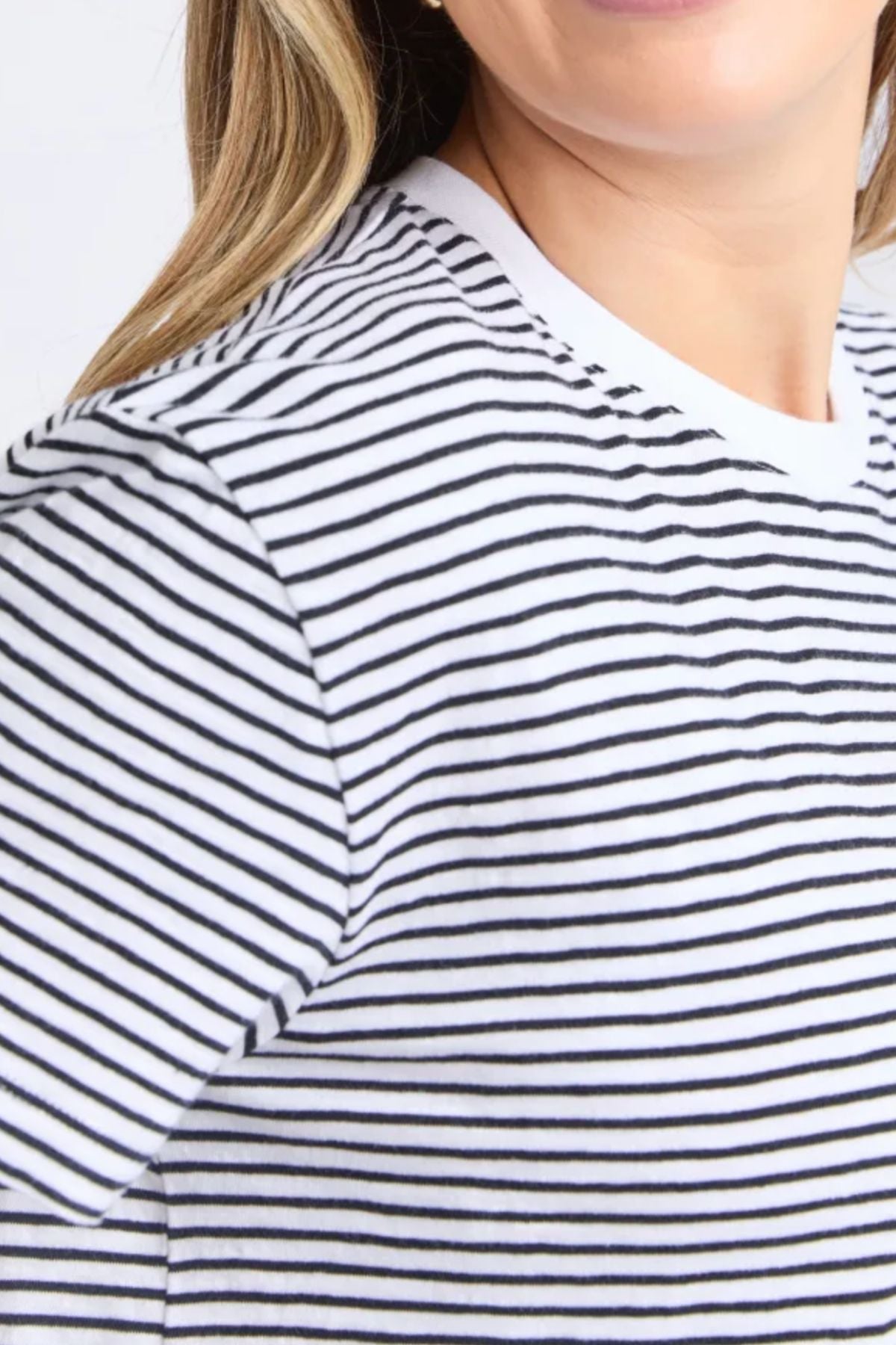 A close-up of a person in the Foxwood Hutch Stripe Teeβwhite with thin black horizontal stripes. They have light skin, long blonde hair, and a partial smile. This relaxed fit tee is perfect for casual wear.