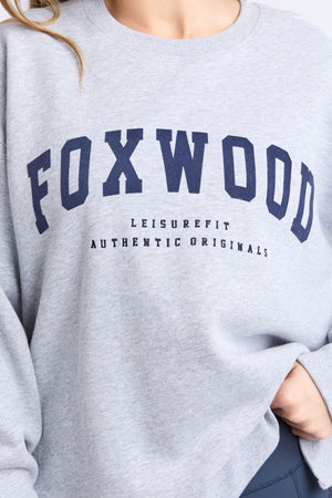 Sporting the Foxwood Intention Crew, a relaxed fit light grey cotton-rich fleece sweatshirt featuring bold navy "FOXWOOD" lettering and "LEISUREFIT AUTHENTIC ORIGINALS" printed underneath.