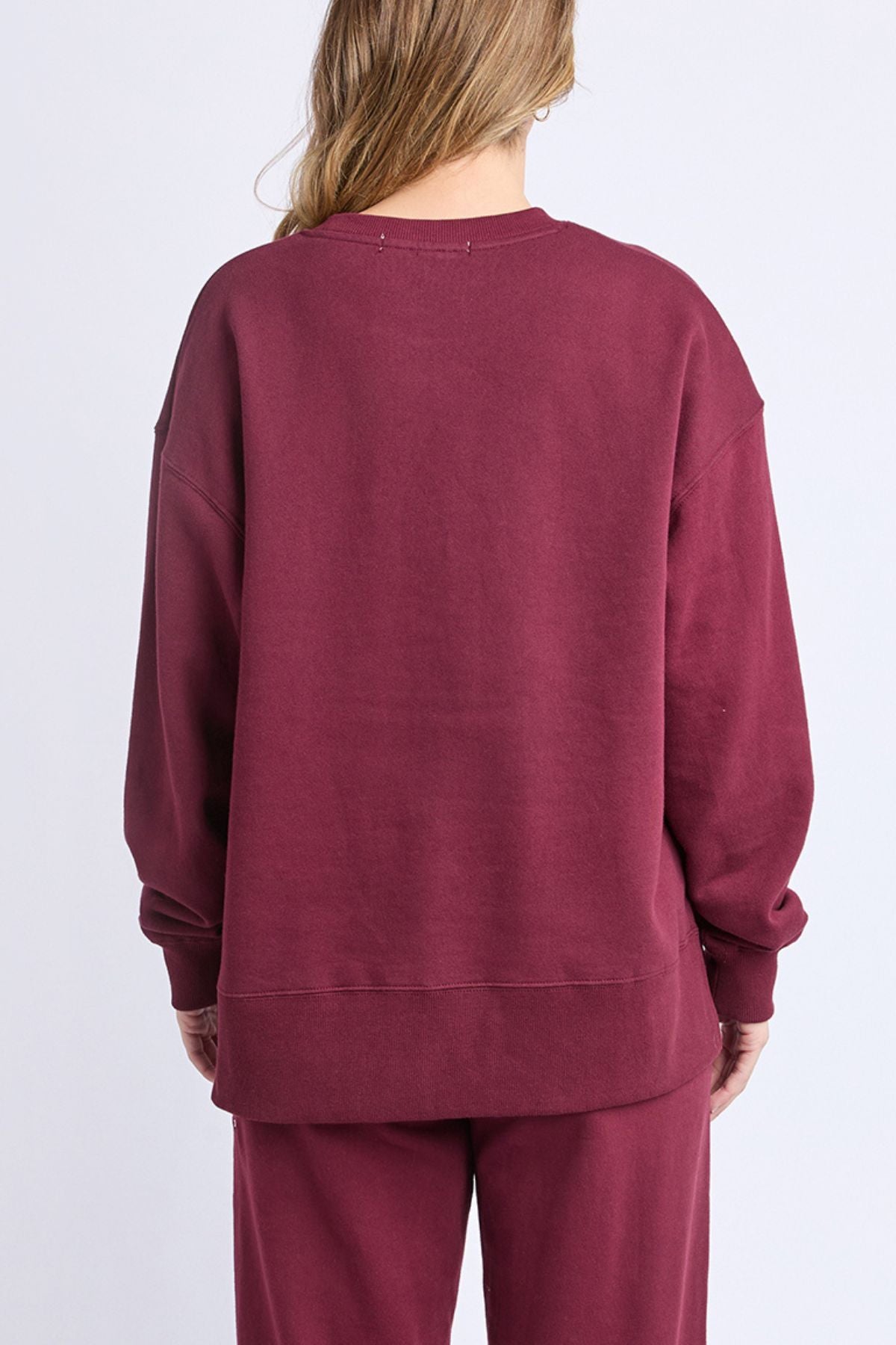 A person with long, light brown hair is seen from behind wearing a relaxed fit Foxwood Intention Crew in maroon cotton-rich fleece, paired with matching pants, set against a plain light gray backdrop.