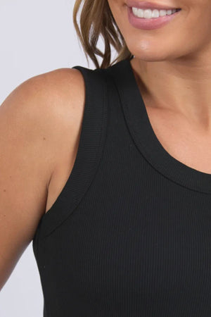 A close-up shows a woman smiling in the Foxwood Iris Tank, featuring black ribbed stretch fabric, with her wavy hair draped to the side and part of her shoulder visible.