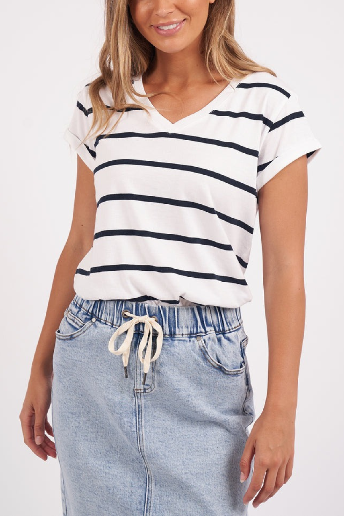 A person wearing the Foxwood Manly Stripe Vee Tee, a white and black yarn-dyed stripe T-shirt made of soft Pima cotton jersey, and a light denim skirt with a drawstring stands against a plain background.