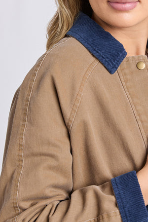 A close-up of a person wearing the Foxwood Colwood Jacket, showcasing its blue corduroy contrast collar and gold snap buttons. Part of the face and upper body is visible, emphasizing the jacket’s sporty, distinctive details.