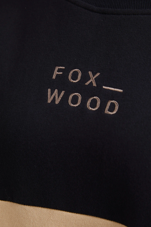 Close-up of a black cotton fleece fabric embroidered with "FOX WOOD" in beige thread. Its smooth texture boosts comfort, with centered embroidery reflecting the Foxwood Offhand Crew style essence.