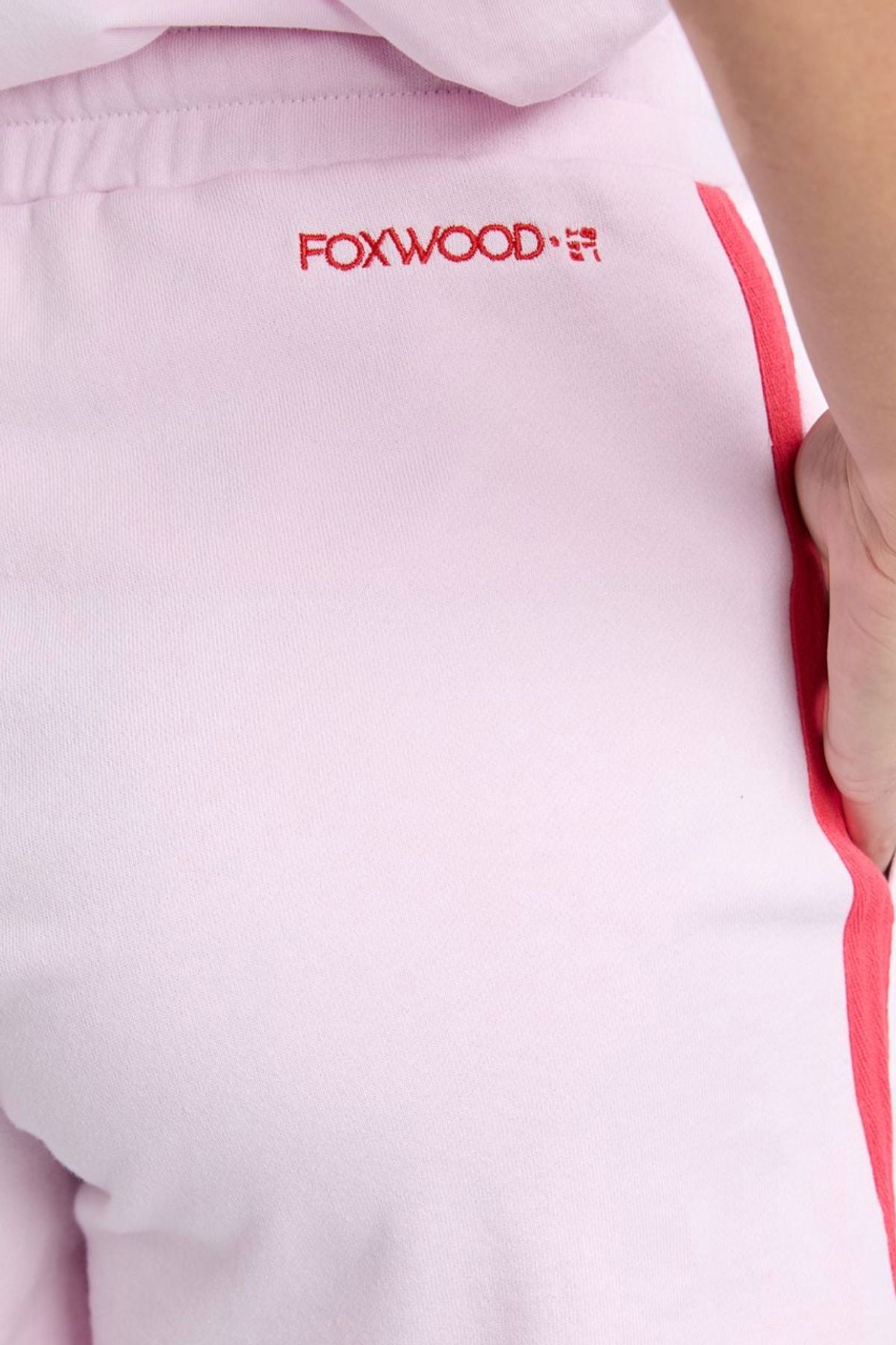 Close-up of a person wearing the Foxwood Palermo Short in light pink with red stripes and "FOXWOOD" embroidered on the back. Their hand rests on their hip, highlighting an easy, relaxed summer style.