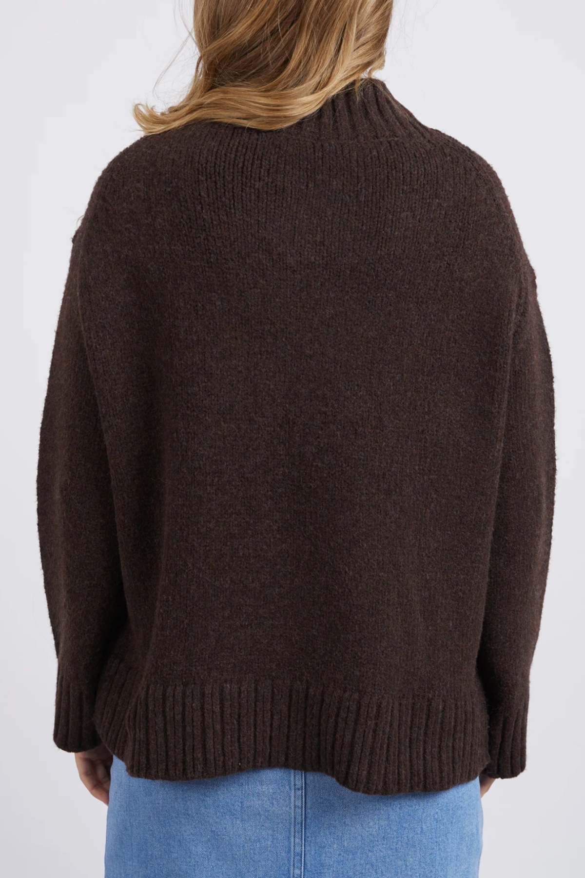 A person with light brown hair, seen from behind, wears the Foxwood Pepper Knit in dark brown and a light blue denim skirt—an ideal outfit for casual occasions.