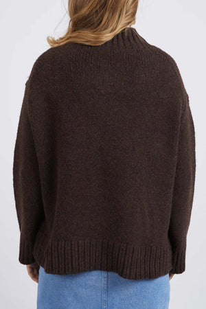 A person with light brown hair, seen from behind, wears the Foxwood Pepper Knit in dark brown and a light blue denim skirt—an ideal outfit for casual occasions.