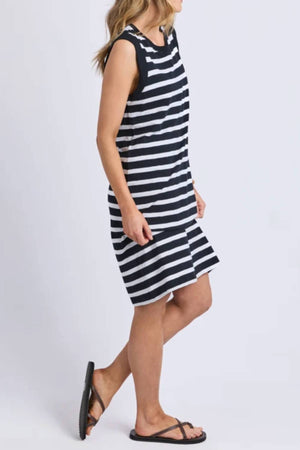 A woman wears the Foxwood Reform Stripe Dress, a sleeveless, knee-length dress featuring horizontal black and white stripes, as she stands sideways with her hair down and in black sandals against a plain white background.