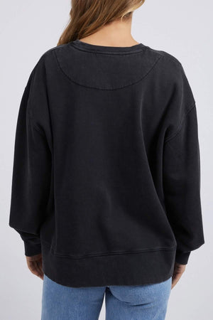 Facing away, a person with long hair wears a loose-fitting Foxwood Rosa Crew sweatshirt made of 100% cotton and light blue jeans, with subtle chest print details. The background is plain and light-colored.