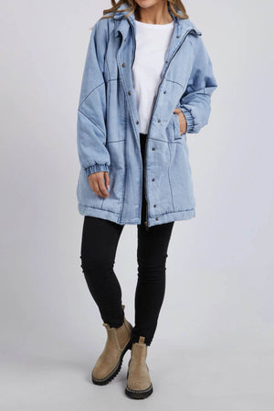 A person in a light blue Foxwood Rosalee Longline Jacket, white t-shirt, black skinny pants, and tan ankle boots stands against a plain light background with their face partially out of frame.