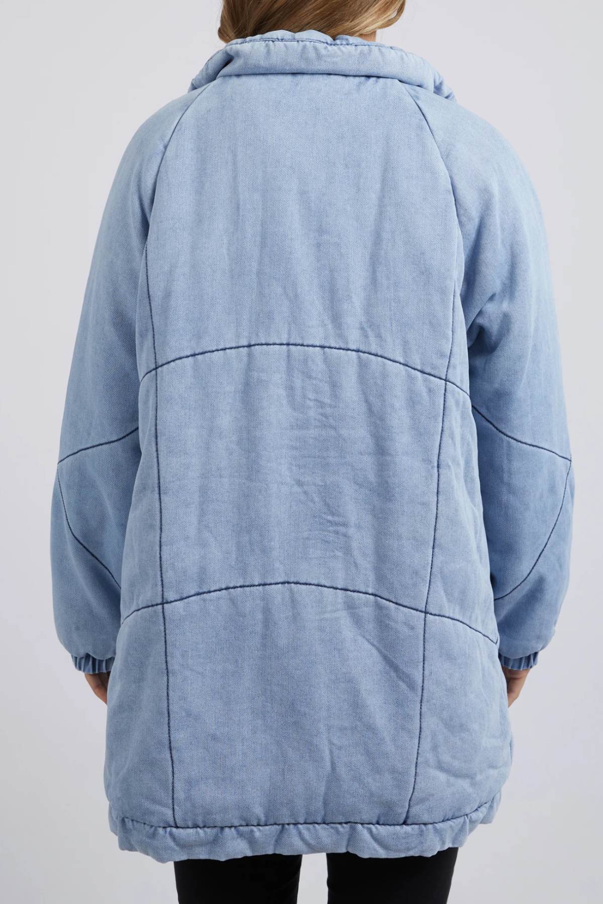 Seen from the back, a person wears the Foxwood Rosalee Longline Jacket—a loose-fit, light blue 100% cotton quilted jacket with visible dark stitching lines. Their arms rest relaxed by their sides.