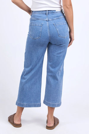 A person wearing the Foxwood Sarah Crop Jean in light blue, high-rise, wide-leg stretchy denim and brown sandals stands with their back to the camera against a plain white background.