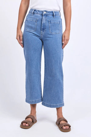 Someone wears the Foxwood Sarah Crop Jean, a high-rise wide-leg style with large front pockets, paired with a white top and brown sandals, standing against a plain light background.
