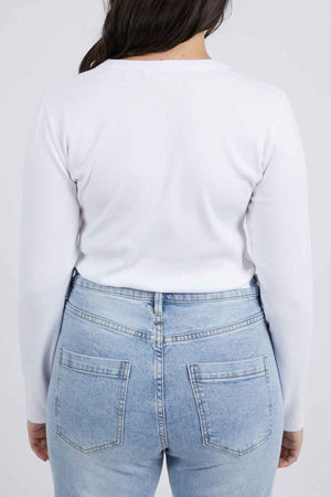 A person with long dark hair is shown from behind, wearing a white Foxwood Scoop Long Sleeve Rib and light blue denim jeans with visible back pockets. The background is plain white.