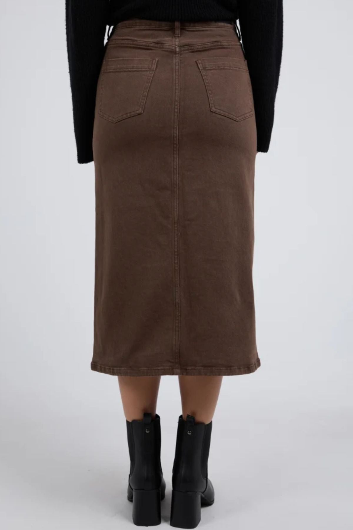 Someone wearing the Foxwood Scout Midi Skirt—brown, high-waisted, midi-length with back pockets—and black ankle boots, shown from behind against a plain gray background.