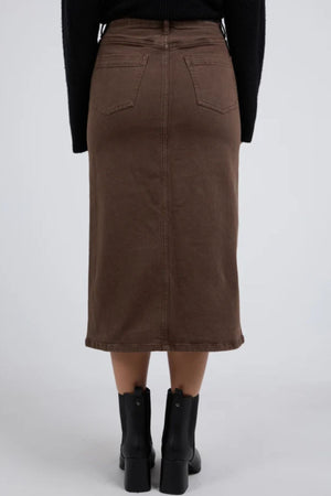 Someone wearing the Foxwood Scout Midi Skirt—brown, high-waisted, midi-length with back pockets—and black ankle boots, shown from behind against a plain gray background.