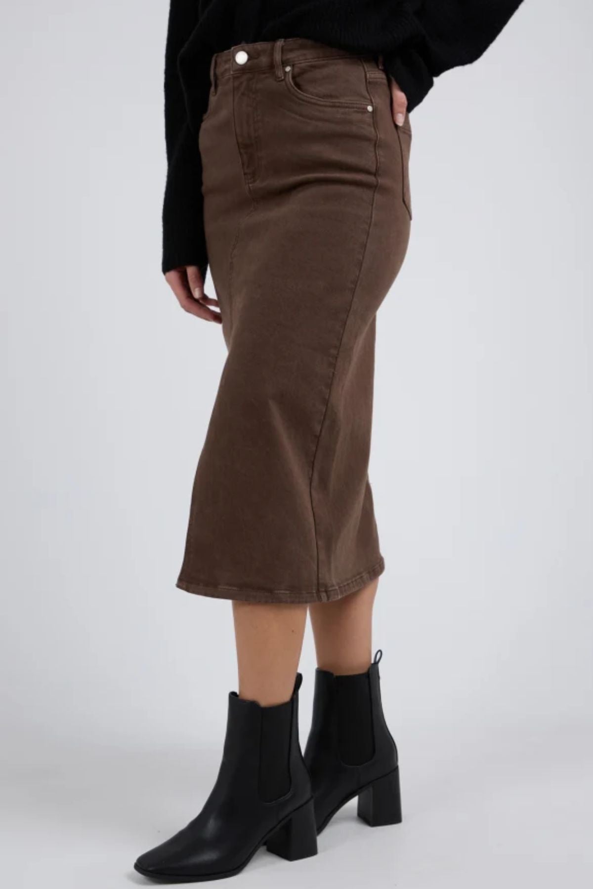 A person wearing the Foxwood Scout Midi Skirt in dark brown, a black top, and black heeled ankle boots stands against a plain light background.