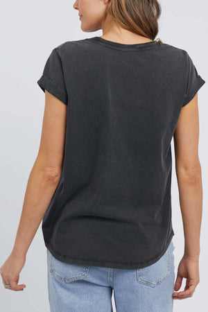 A woman is shown from the back, wearing the Foxwood Signature Tee in dark gray, with short sleeves that are slightly rolled. She has light brown hair and is paired with light blue denim jeans against a plain, light-colored background.