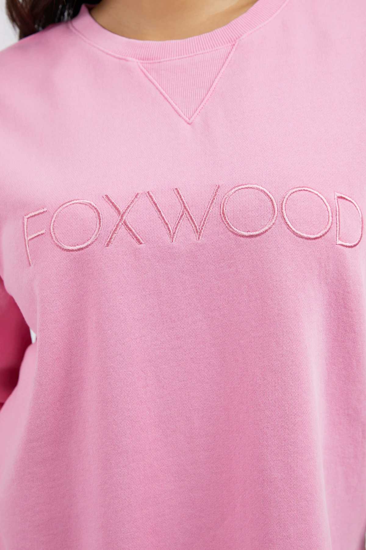 Someone wears the Foxwood Simplified Crew, a light pink 100% cotton sweatshirt with "FOXWOOD" embroidered across the chest in matching pink thread.