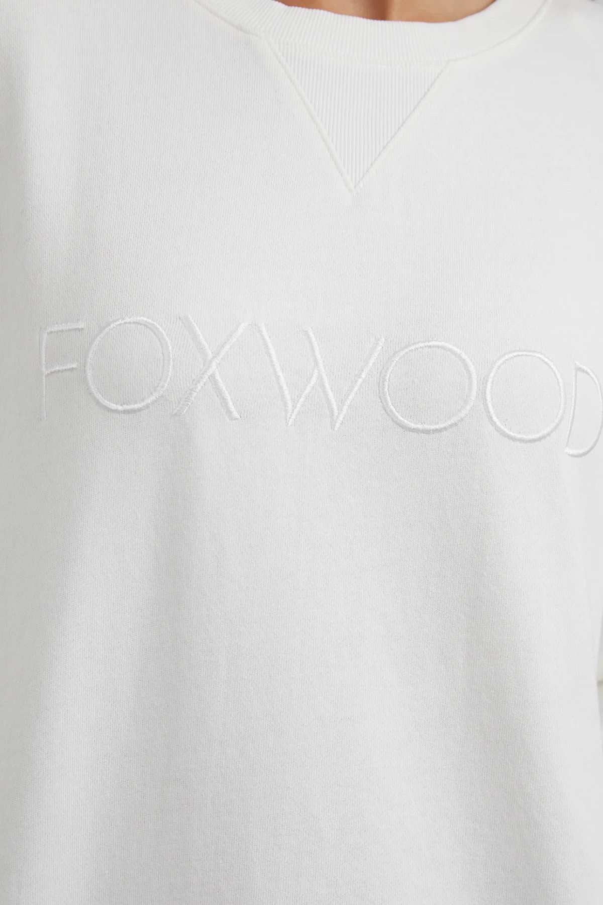 Close-up image of a white or off-white Foxwood Simplified Crew with the word "FOXWOOD" embroidered across the chest in subtly raised, matching colored threads.