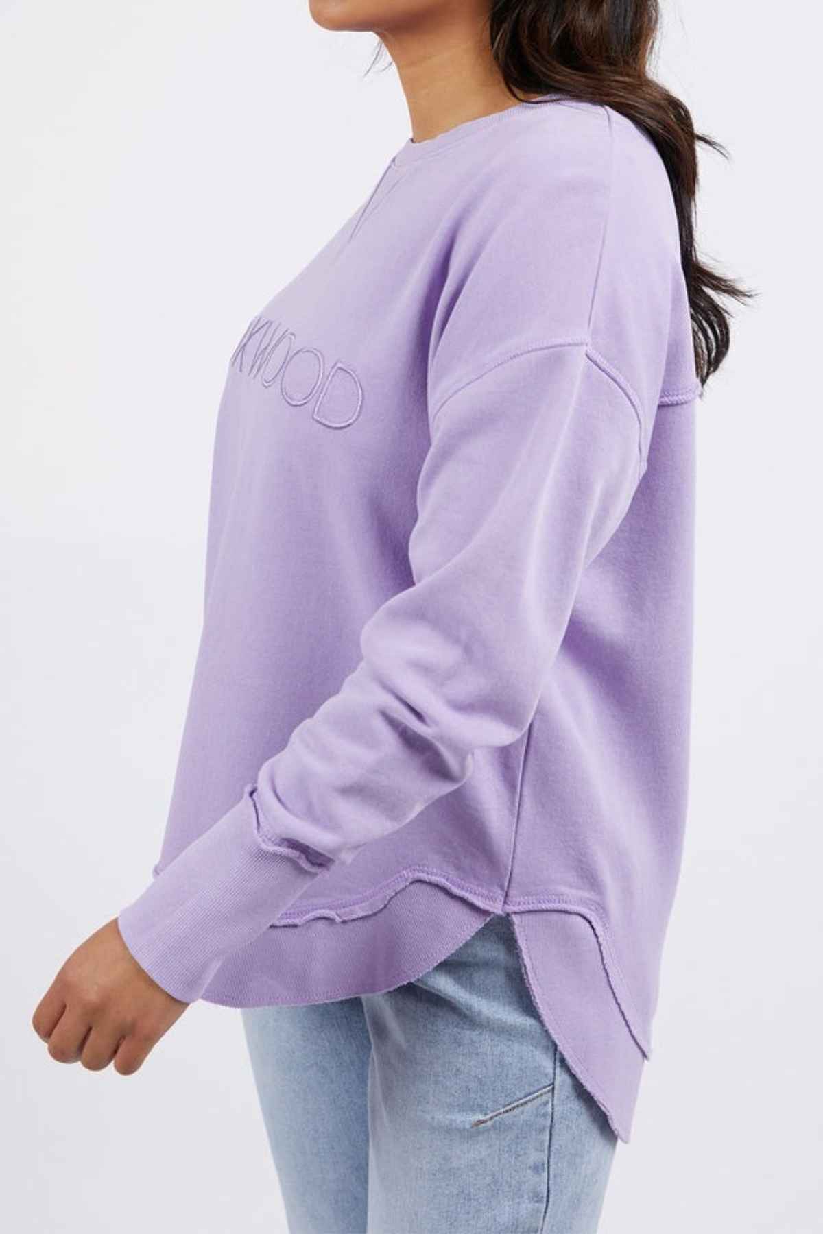 A person in a light purple Foxwood Simplified Crew sweatshirt with a relaxed fit and light blue jeans, standing sideways to the camera against a plain white background.