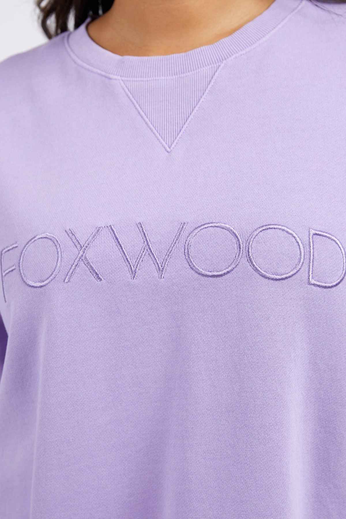A close-up of the Foxwood Simplified Crew, a lavender sweatshirt with "FOXWOOD" embroidered on the chest. Made from 100% cotton, it offers a relaxed fit for ultimate comfort.