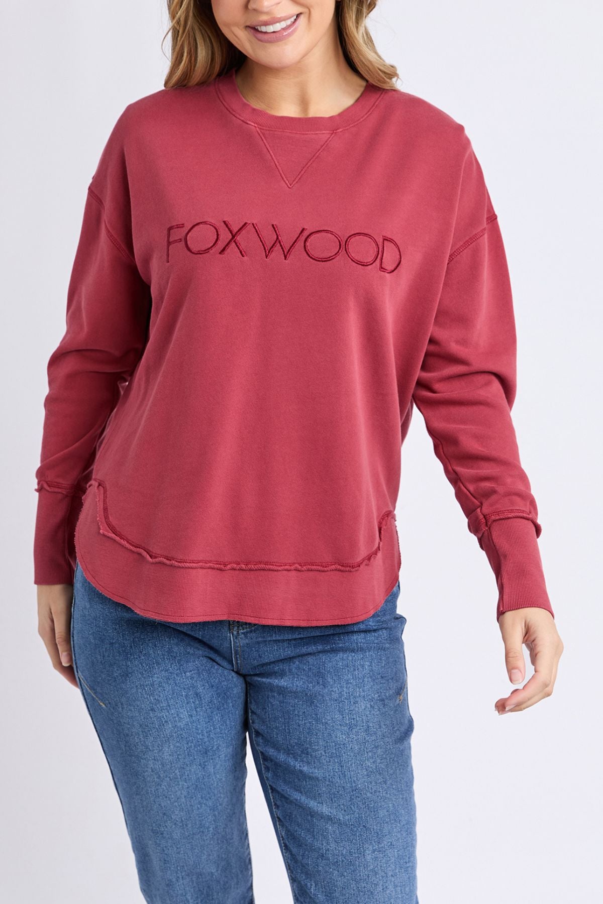 A woman models the Foxwood Simplified Crew, a relaxed fit 100% cotton sweatshirt with "FOXWOOD" embroidery, paired with blue jeans against a plain light background.