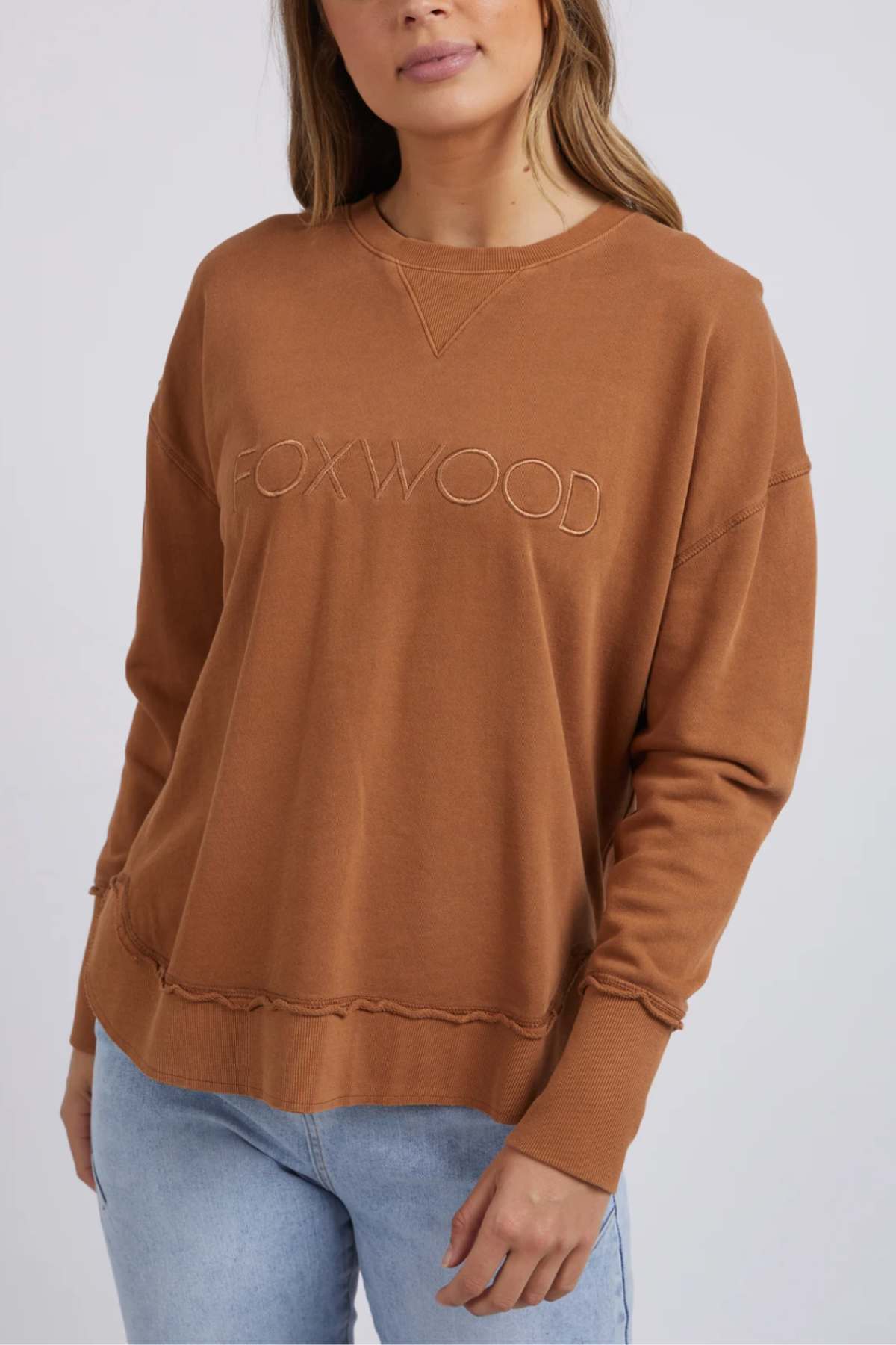 A woman in the Foxwood Simplified Crew, featuring front embroidery and made from 100% cotton for comfort, pairs it with light blue jeans against a plain light background.