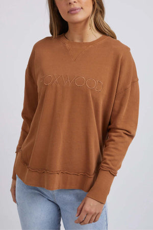 A woman in the Foxwood Simplified Crew, featuring front embroidery and made from 100% cotton for comfort, pairs it with light blue jeans against a plain light background.