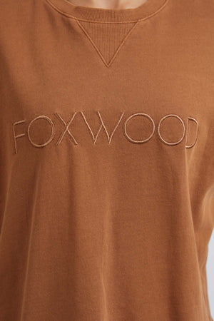 Close-up of the Foxwood Simplified Crew, a brown sweatshirt made from 100% cotton, featuring bold "FOXWOOD" embroidery in large capital letters across the chest.