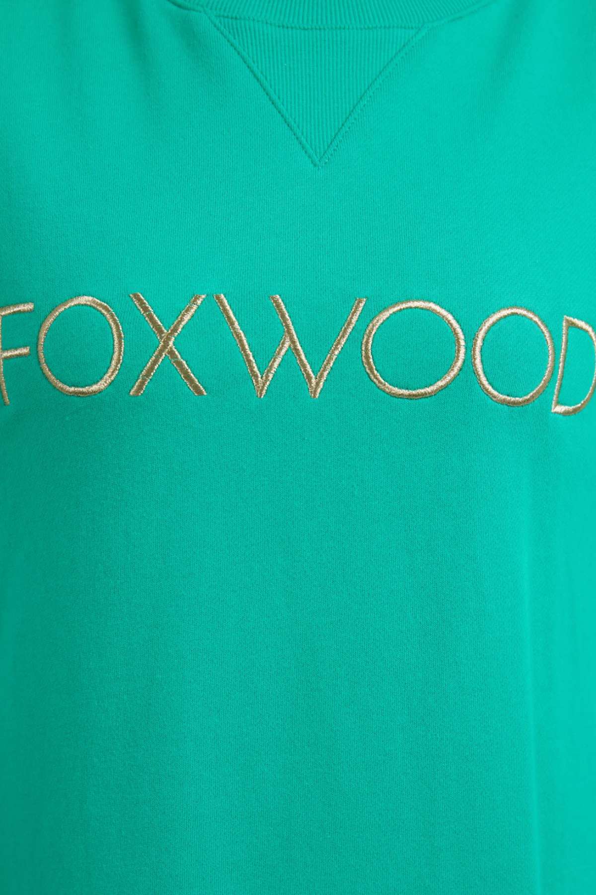 Close-up of the Foxwood Simplified Metallic Crew, a green cotton sweatshirt featuring "FOXWOOD" embroidered in gold across the center.
