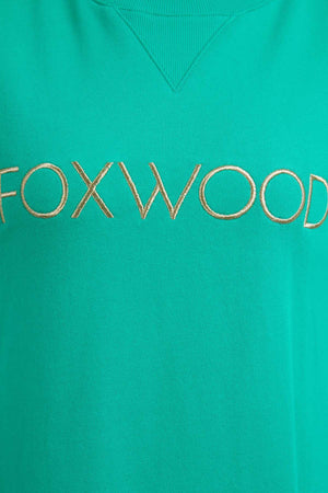 Close-up of the Foxwood Simplified Metallic Crew, a green cotton sweatshirt featuring "FOXWOOD" embroidered in gold across the center.